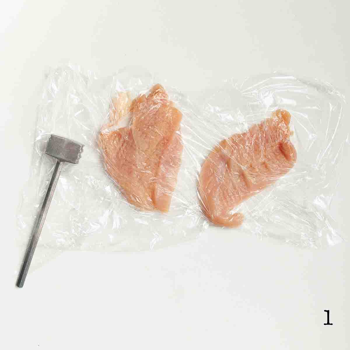 Two chicken cutlets pounded between sheets of plastic.