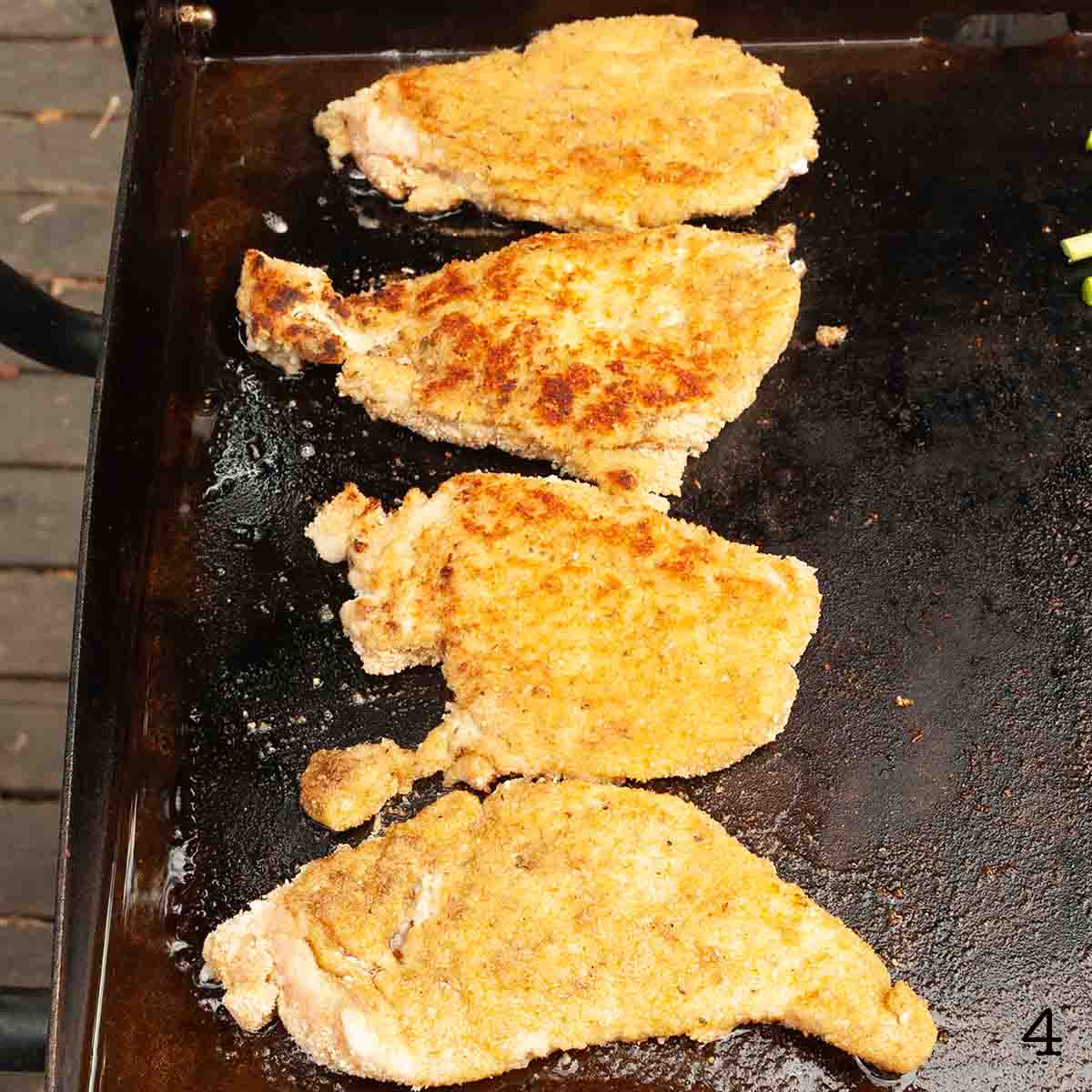Four chicken cutlets cooking on a griddle.