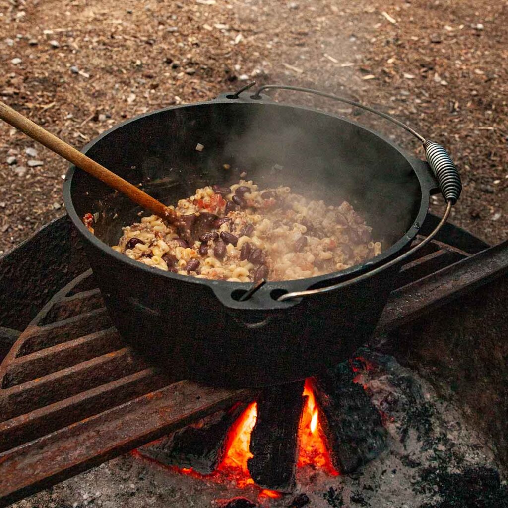 A pot of campfire chili mac over a campfire.