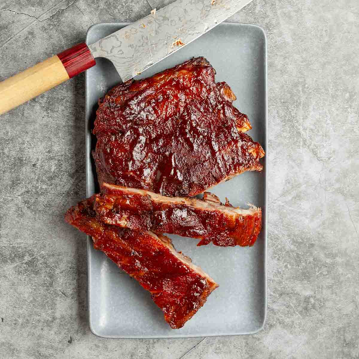 A partially cut rack of grilled spare ribs on a platter with a knife.