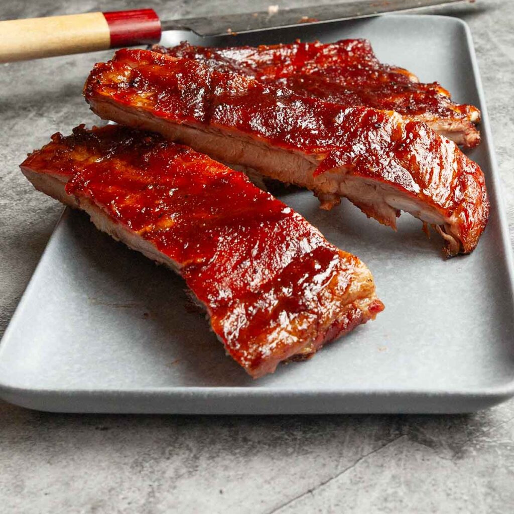 A partially cut rack of grilled spare ribs on a platter with a knife.