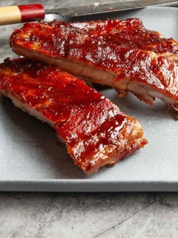 A partially cut rack of grilled spare ribs on a platter with a knife.