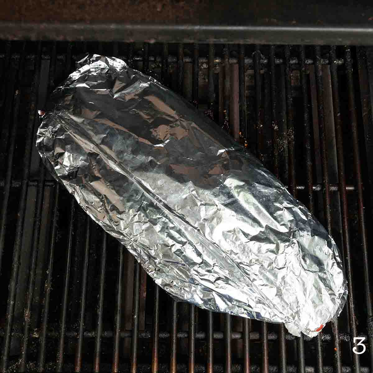 A rack of ribs wrapped in foil on the grill.