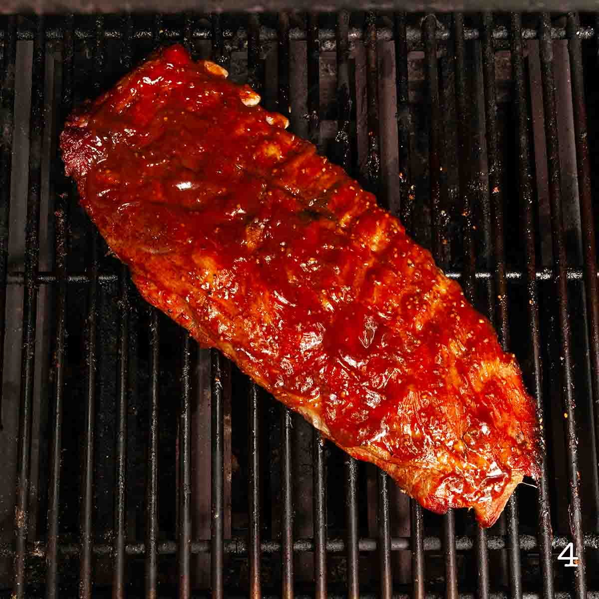 A rack of ribs coated with BBQ sauce on the grill.