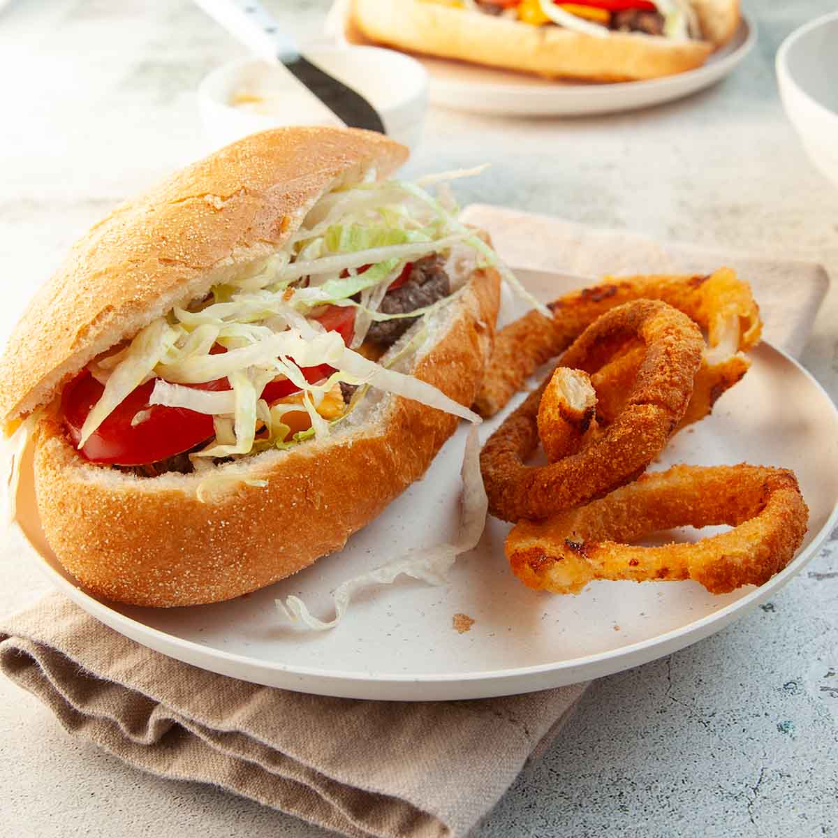 A Blackstone chopped cheese sandwich with lettuce and tomato and onion rings on the side.