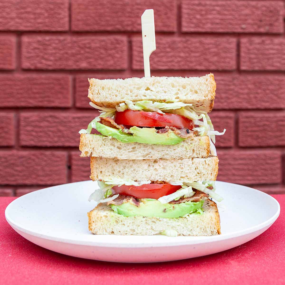 Two sandwich halves with bacon, tomato, lettuce, and avocado, stacked on top of each other.