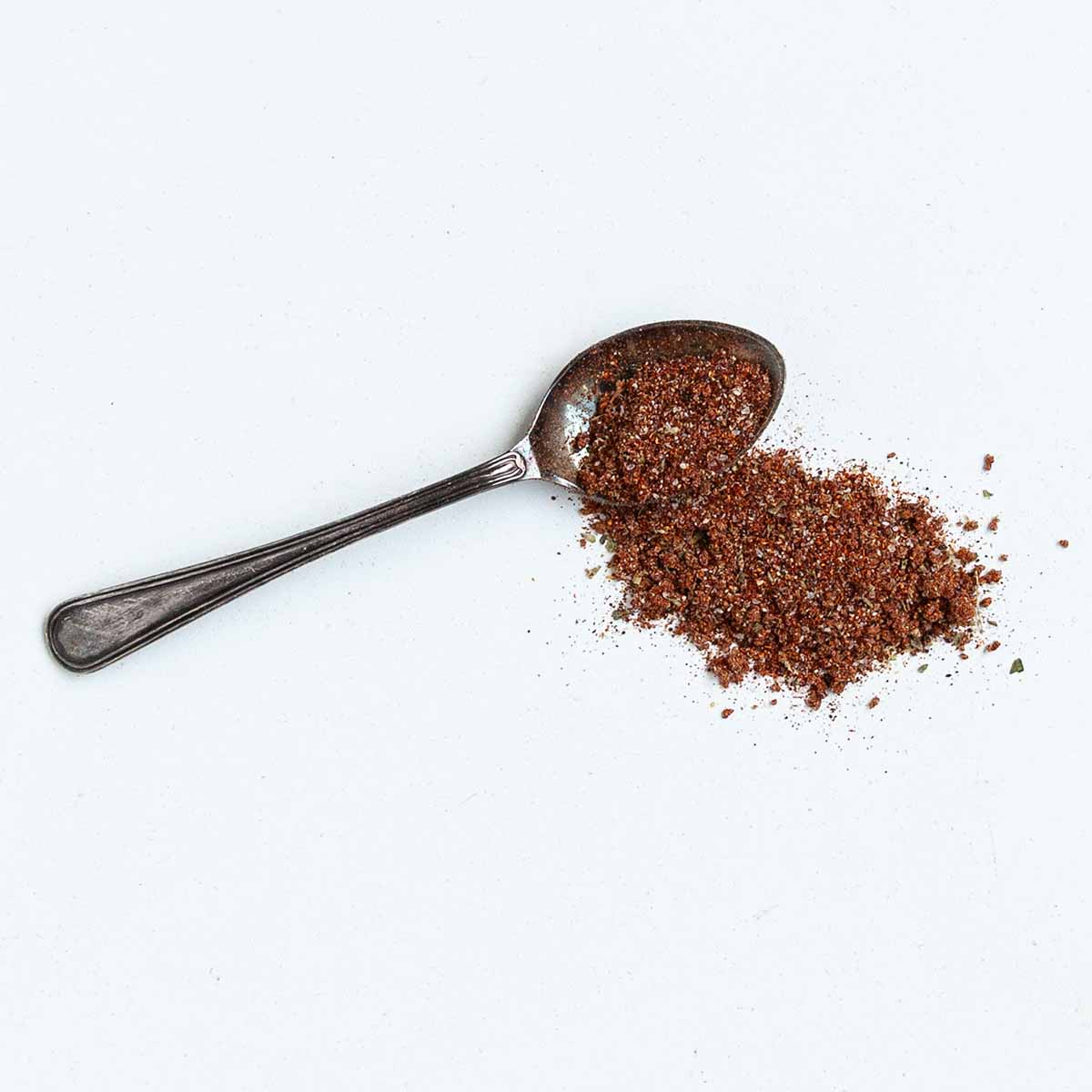 A spoonful of BBQ rub on a white surface.