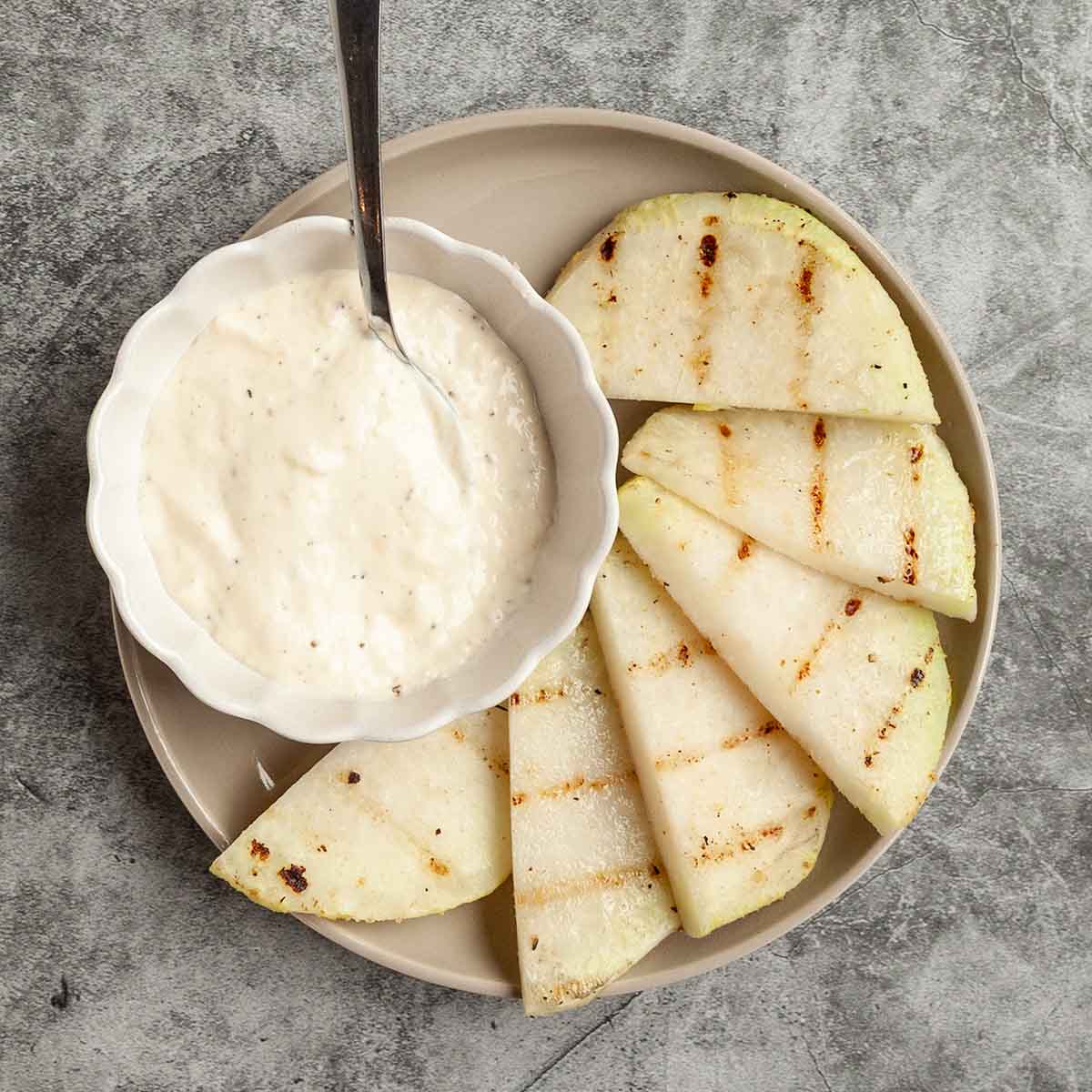 Half-moon slices of kohlrabi with a bowl of dip on the side.