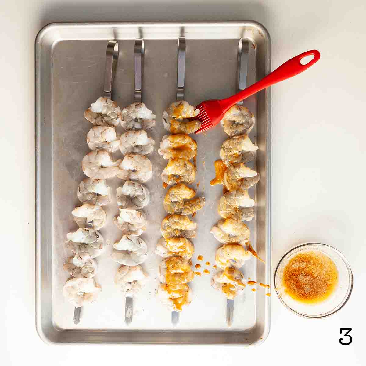 Shrimp skewers being brushed with seasoned melted butter.