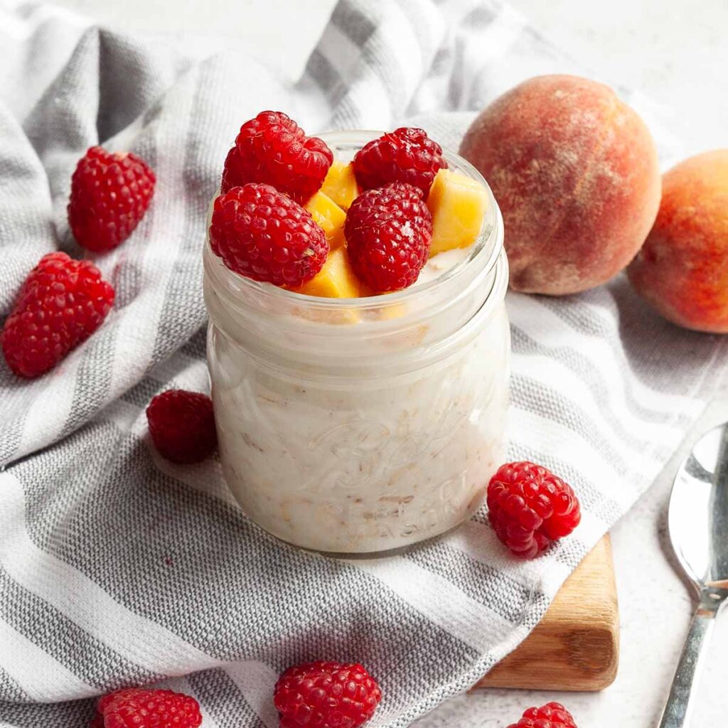 A jar of overnight oats topped with peaches and raspberries.