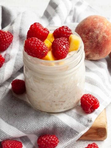 A jar of overnight oats topped with peaches and raspberries.