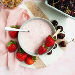 A bowl of strawberry fruit dip with strawberries and cherries scattered around it.