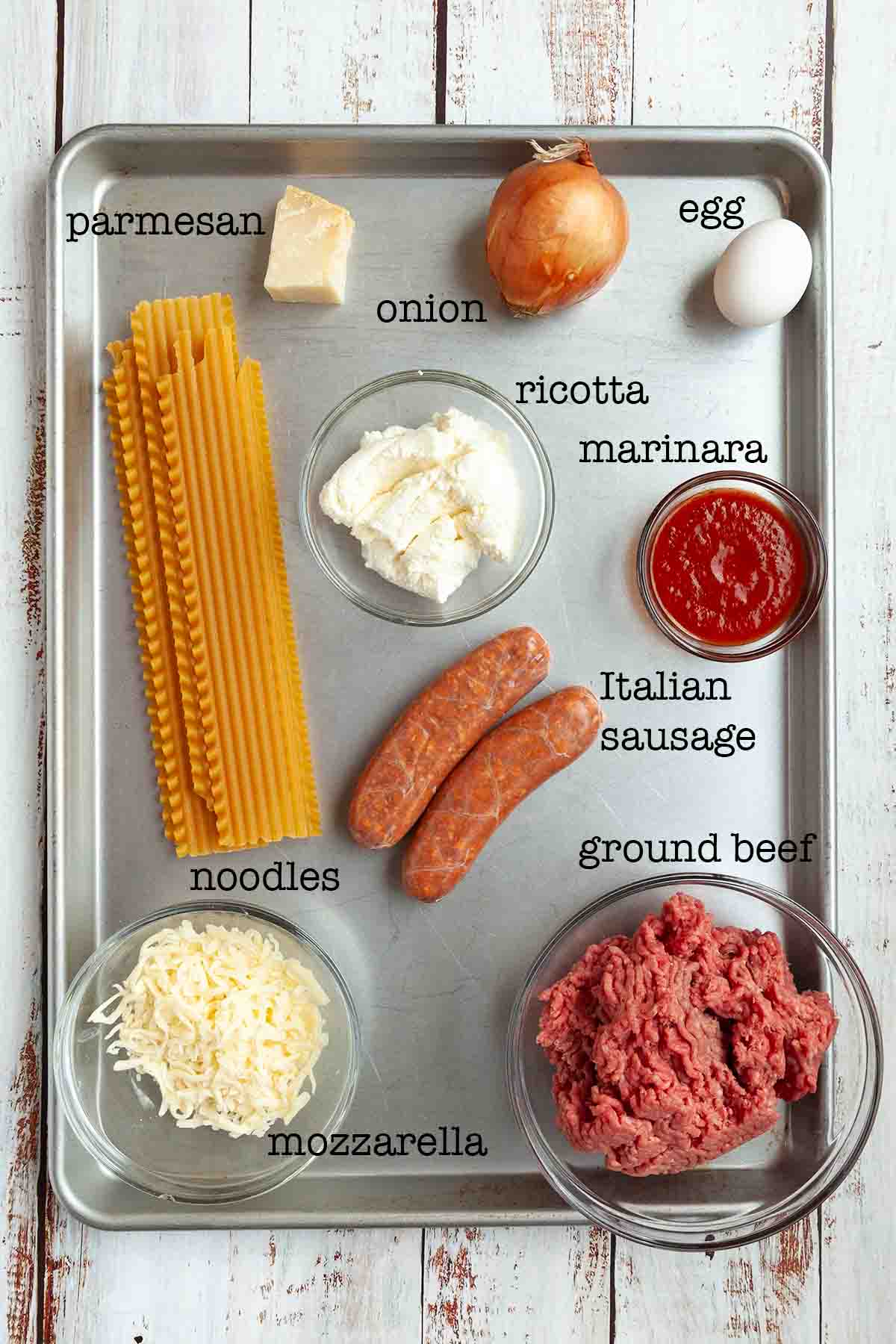 Ingredients for Dutch oven lasagna--parmesan, onion, egg, ricotta, marinara, Italian sausage, ground beef, noodles, and mozzarella.
