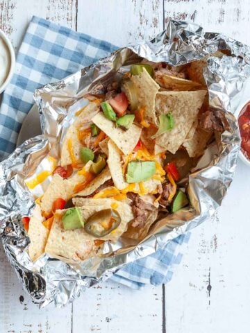 A foil packet of chicken nachos with salsa and sour cream on the side.