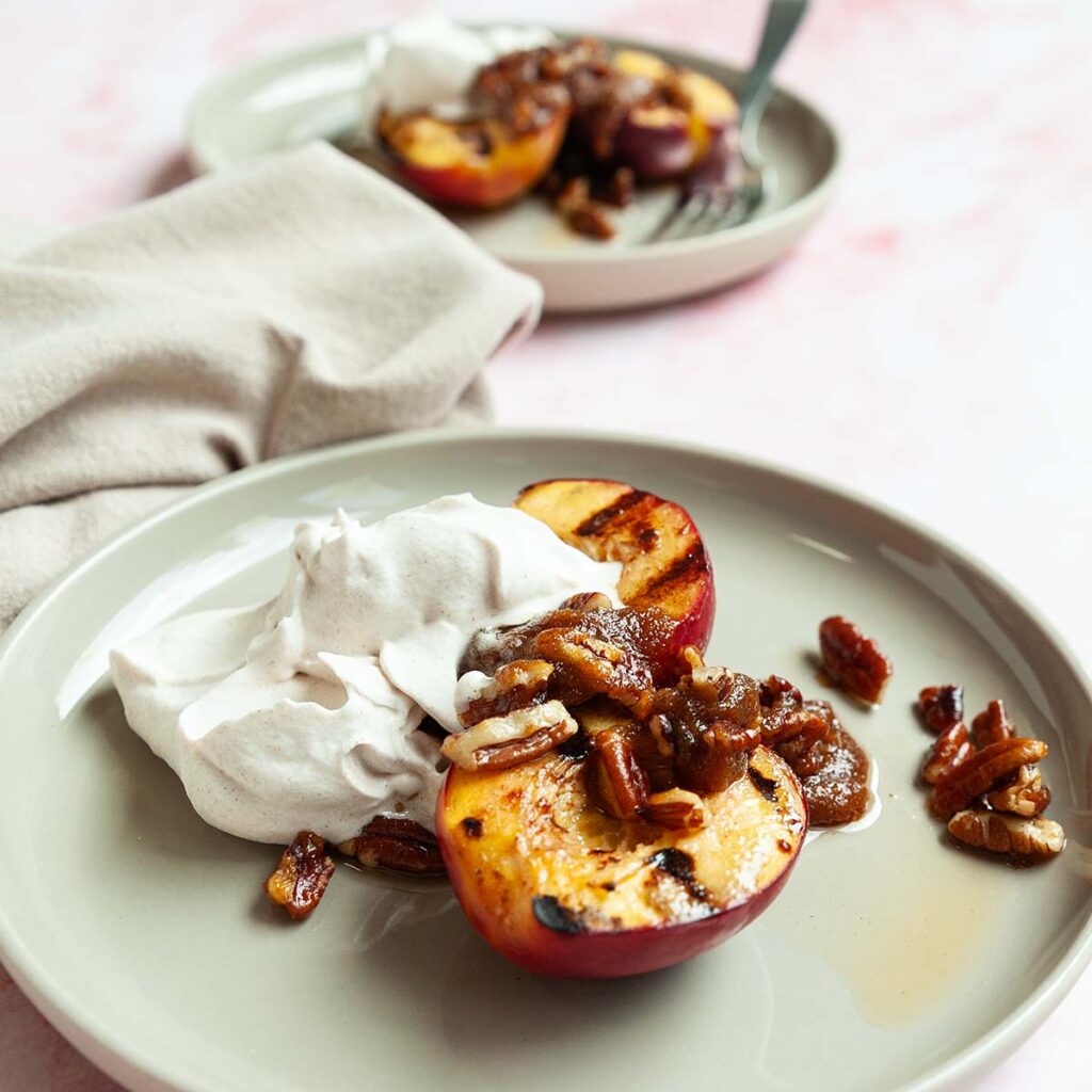 Two plates topped with grilled nectarines, candied pecans, and whipped cream.