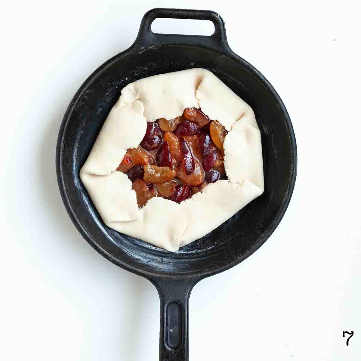 An uncooked plum galette in a cast iron skillet.