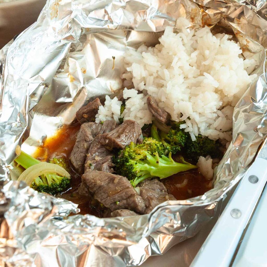 A foil packet with beef, broccoli, and rice.