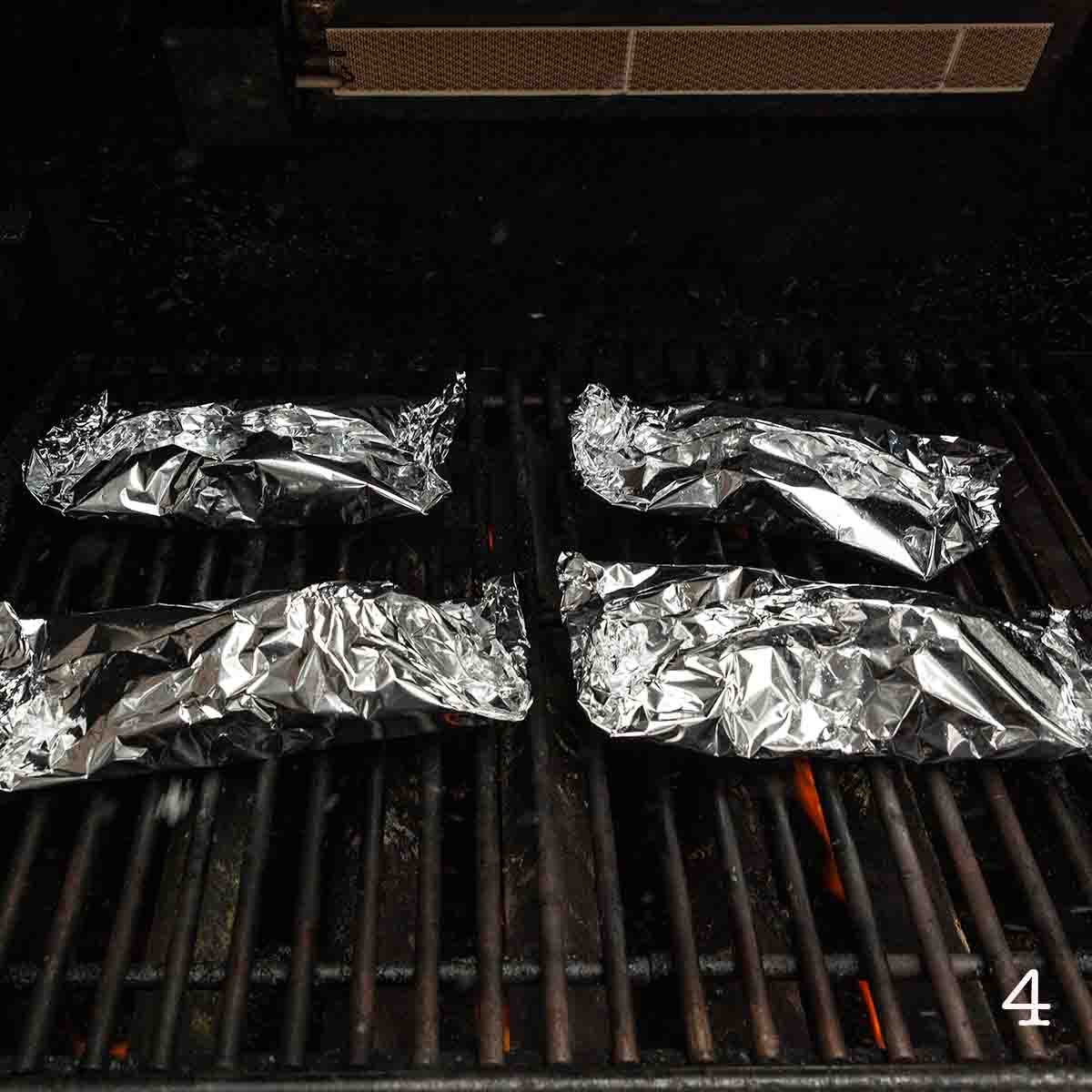 Four foil packets cooking on the grill.