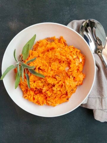 A bowl of mashed sweet potatoes with sage on top.