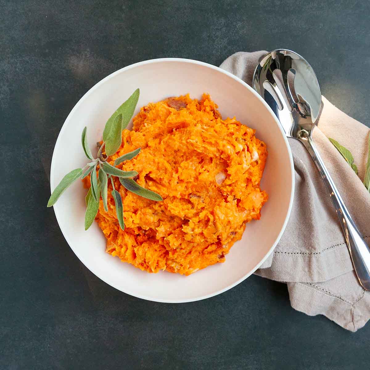 A bowl of mashed sweet potatoes with sage on top.
