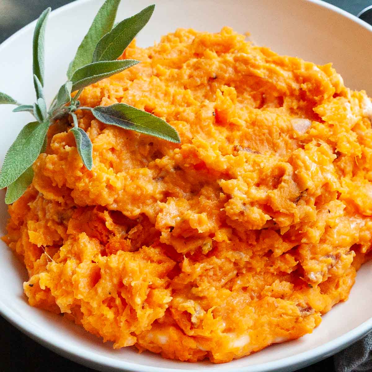 A bowl of mashed sweet potatoes with sage on top.