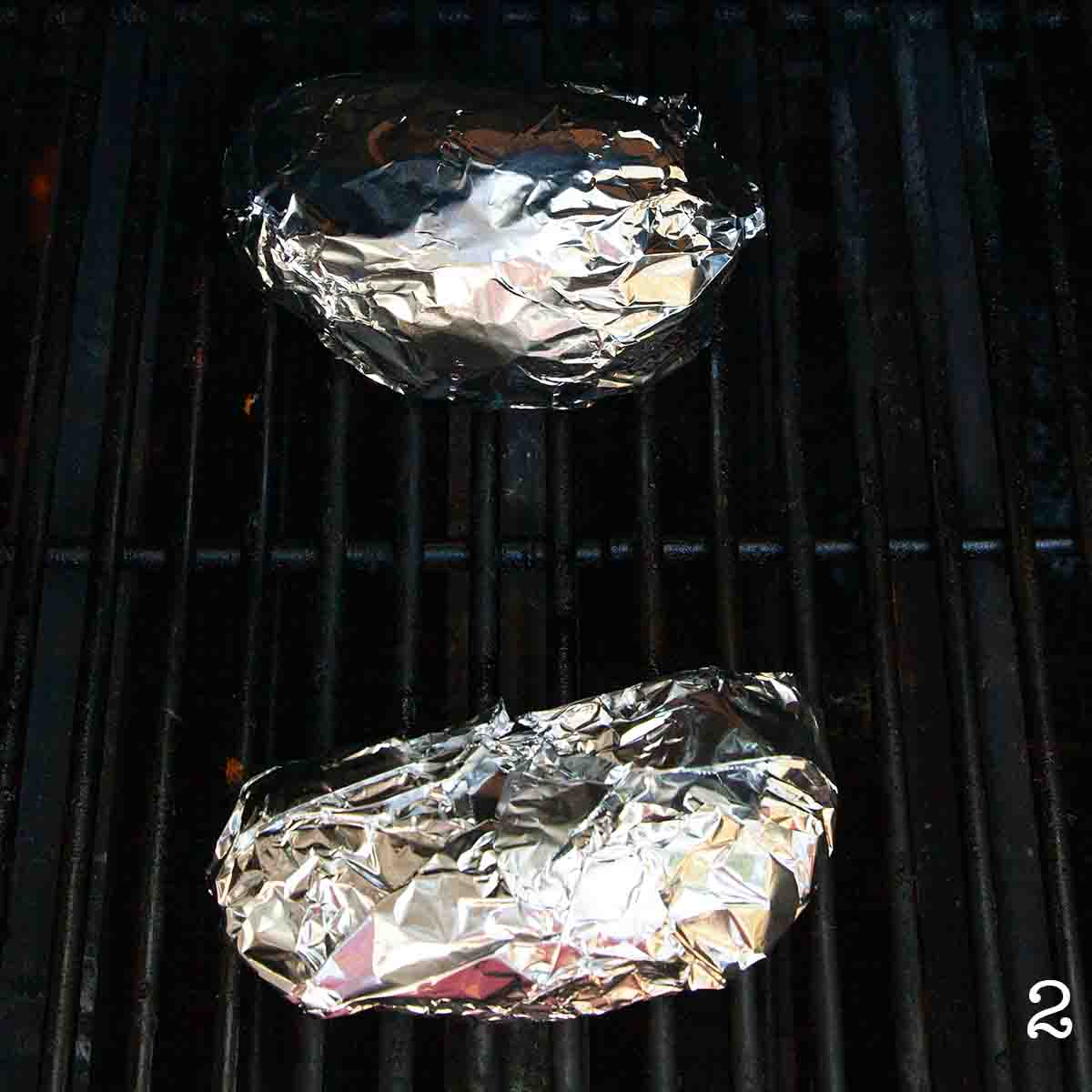Two sweet potatoes in foil on a bbq grill.