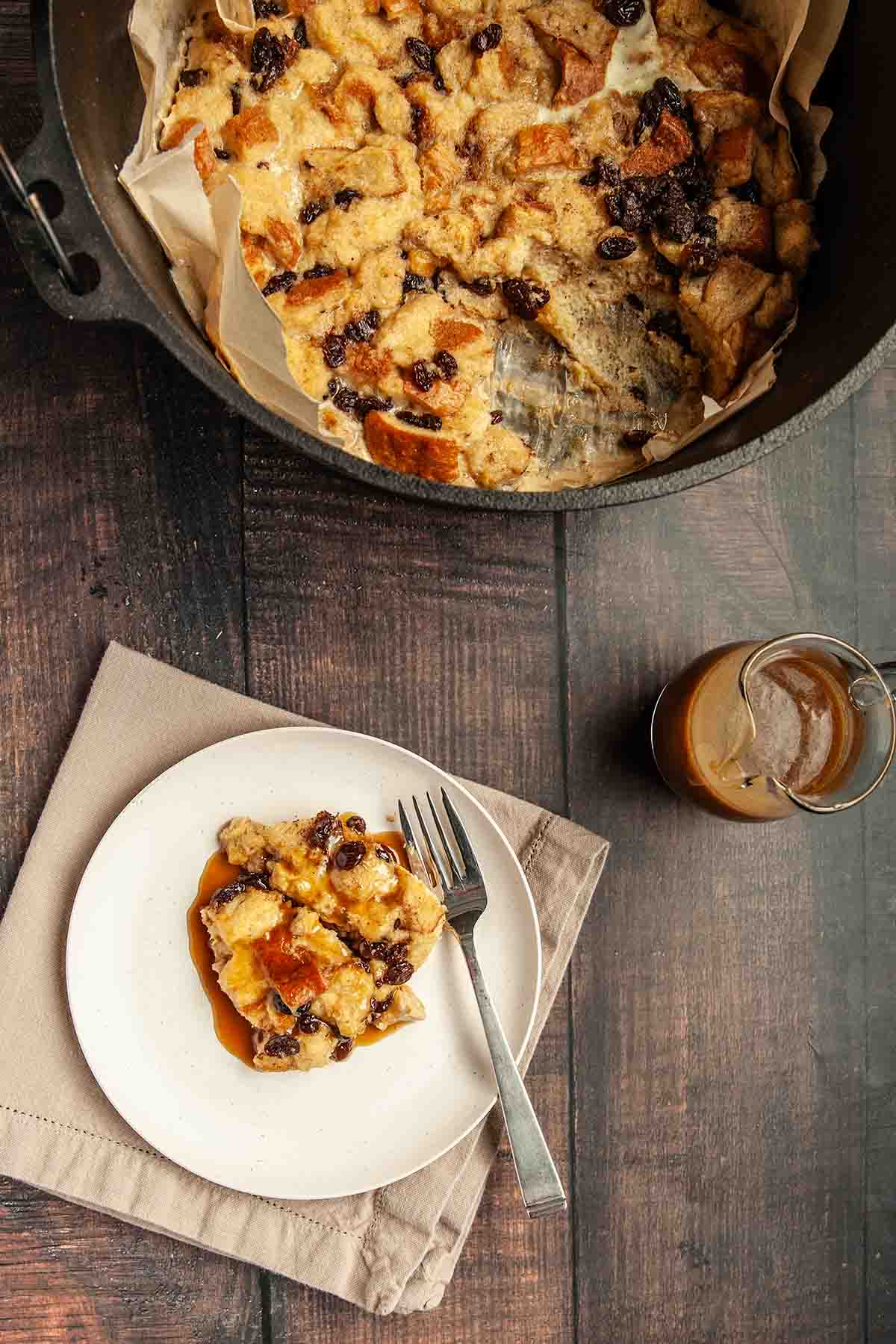A serving of bread pudding on a plate with a Dutch oven nearby.