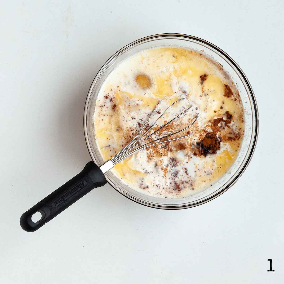 A bowl of liquid with a whisk resting inside.