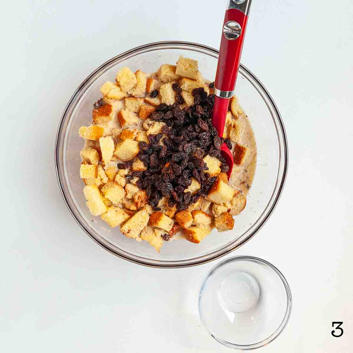 Raisins on top of a bowl of cubed brioche bread.