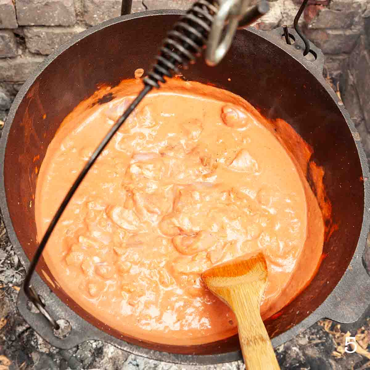 Chicken pieces cooking in a creamy tomato sauce in a Dutch oven.