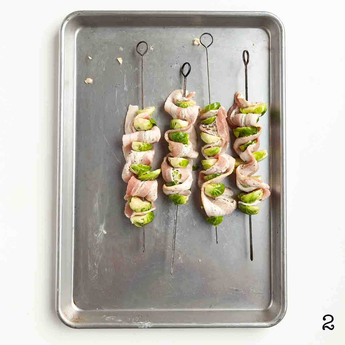 Four uncooked skewers of Brussels sprouts and bacon.