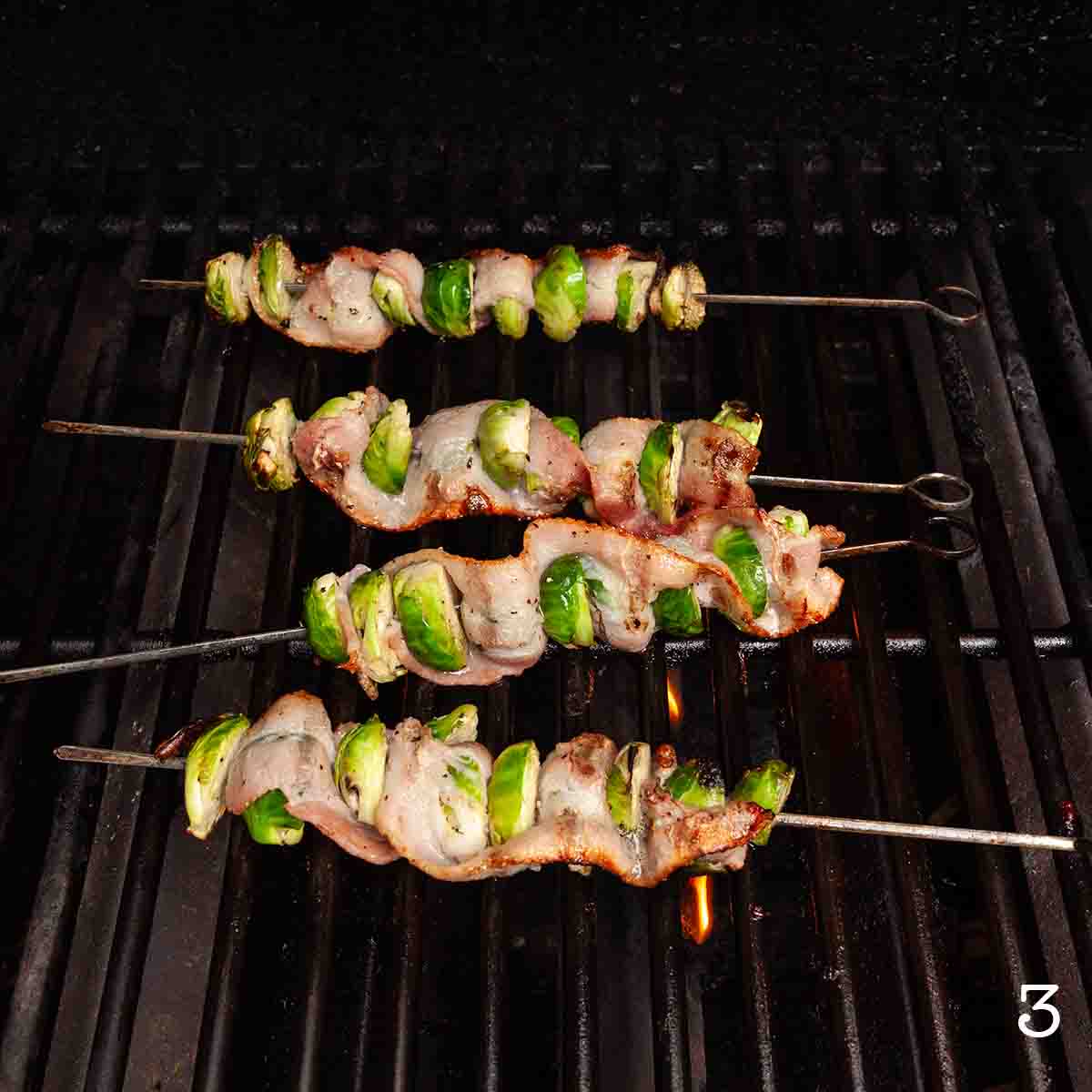 Four Brussels sprouts and bacon skewers cooking on the grill.