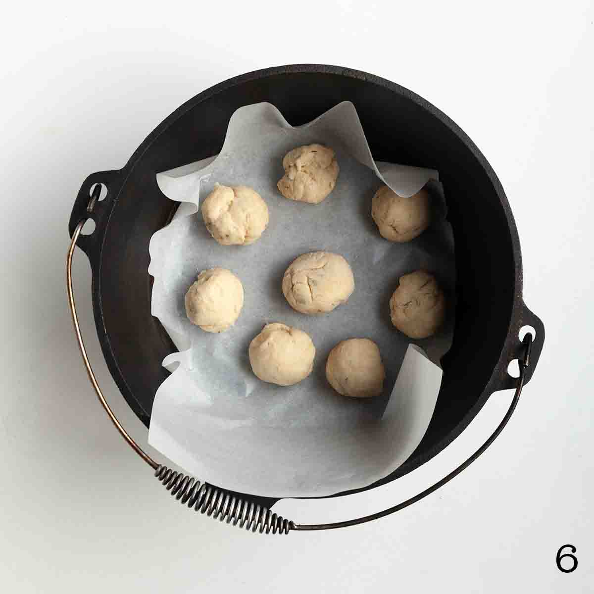 Eight uncooked dough balls in a cast iron Dutch oven.