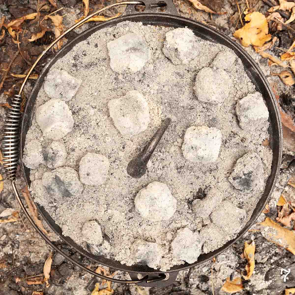 A Dutch oven covered in coals.