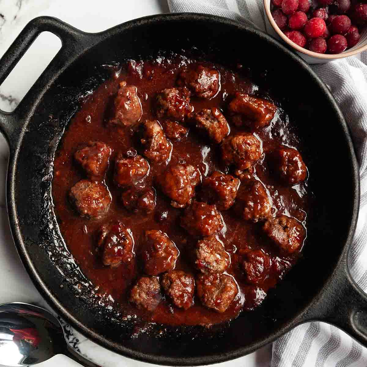 A skillet filled with meatballs in cranberry sauce.