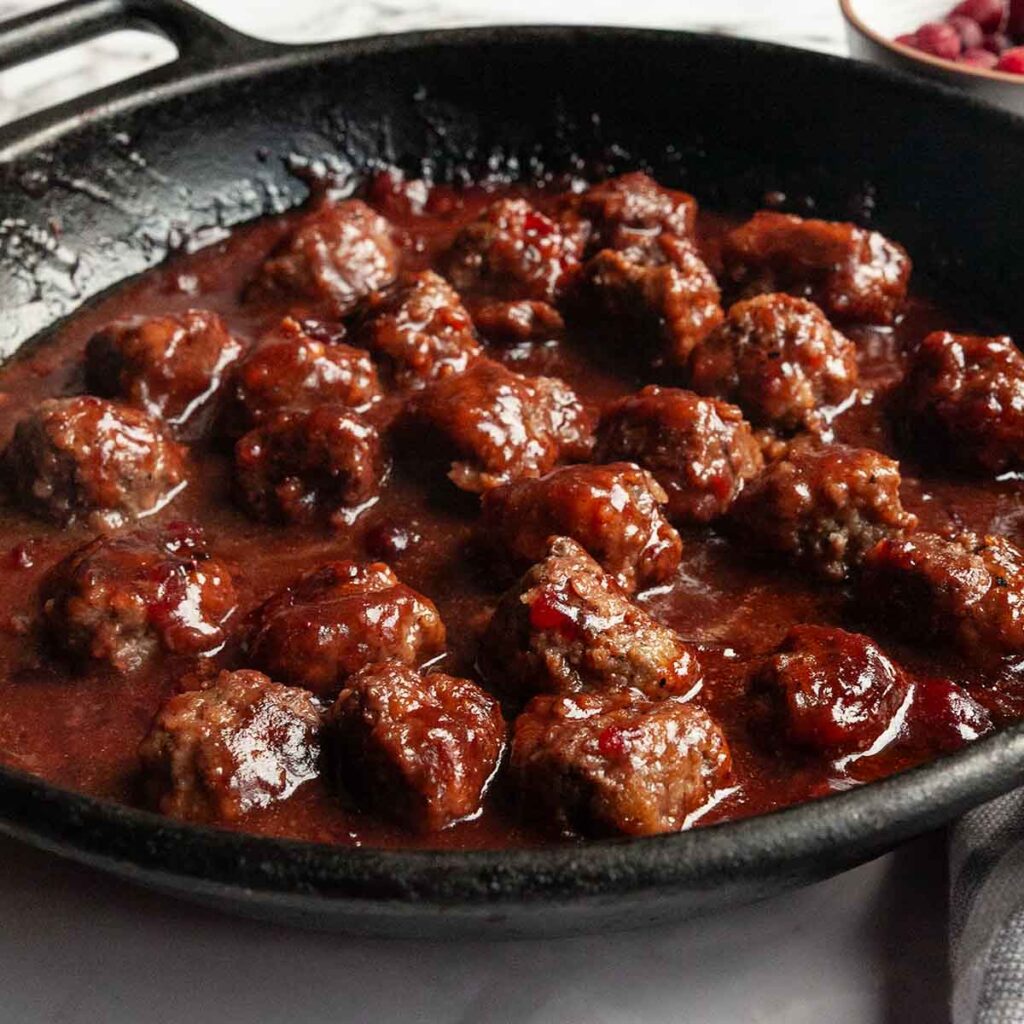 A skillet filled with meatballs in cranberry sauce.