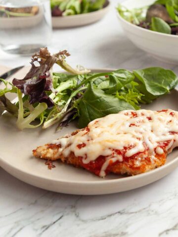 A pieces of chicken parmesan on a plate with mixed greens.