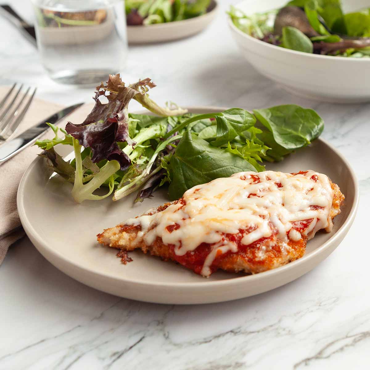 A pieces of chicken parmesan on a plate with mixed greens.