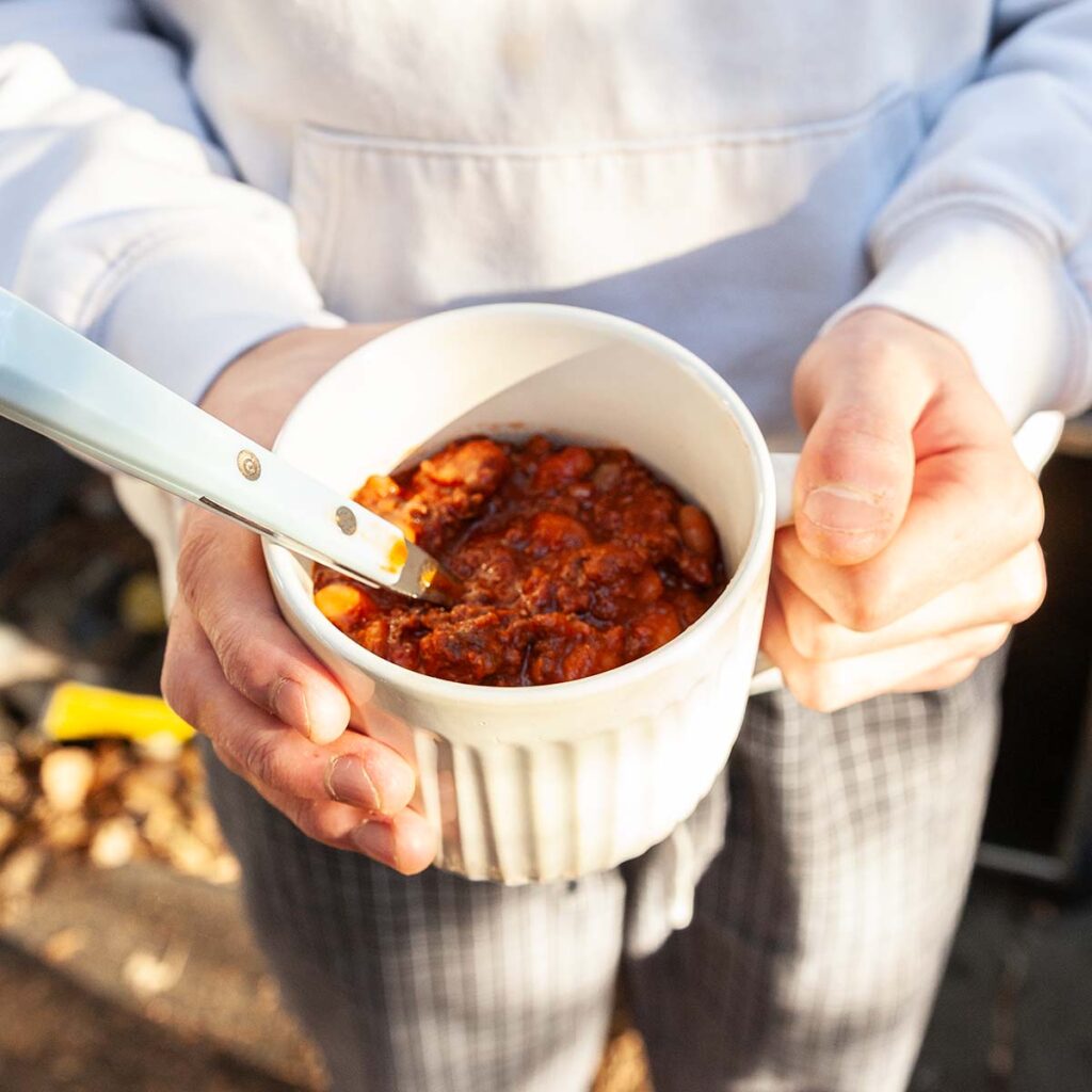 A person holding a mug of chili.