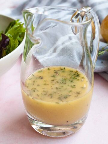 A small glass pitcher half full of lemon thyme vinaigrette.