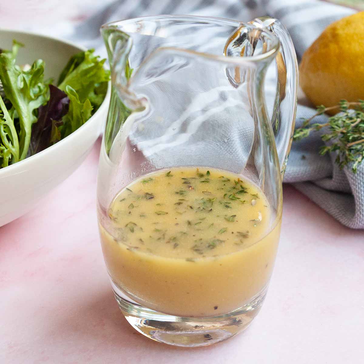 A small glass pitcher half full of lemon thyme vinaigrette.