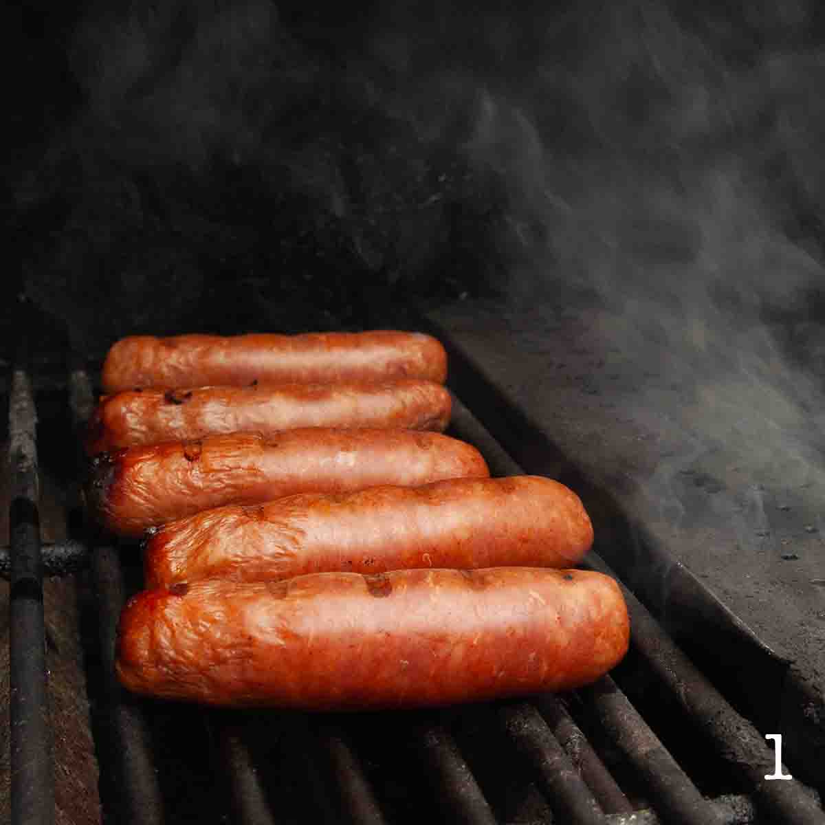 Five sausages on a grill with smoke.
