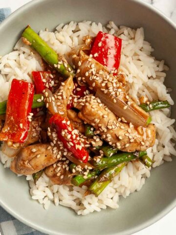 A bowl of chicken, pepper, and asparagus stir fry on top of rice.