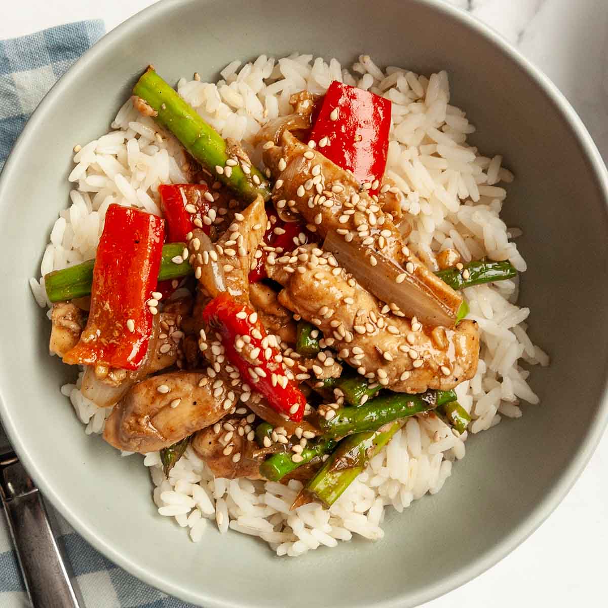 A bowl of chicken, pepper, and asparagus stir fry on top of rice.