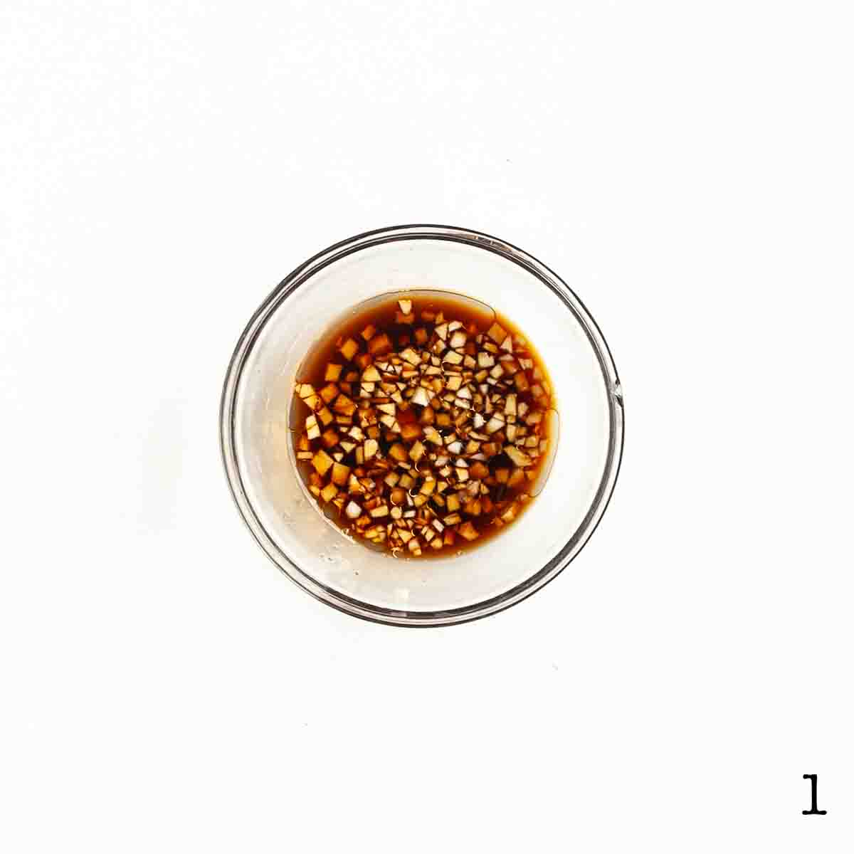 A bowl of soy sauce with chopped ginger and garlic.