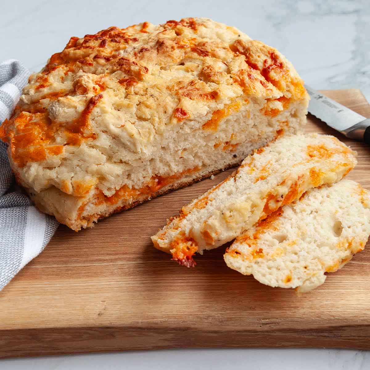 A partially sliced loaf of cheese bread on a cutting board.