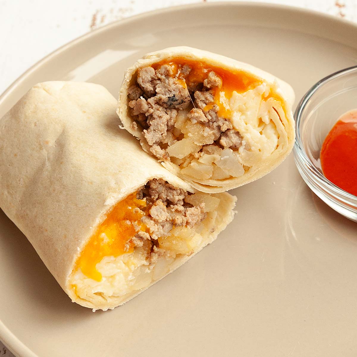 A breakfast burrito cut in half on a plate with hot sauce on the side.