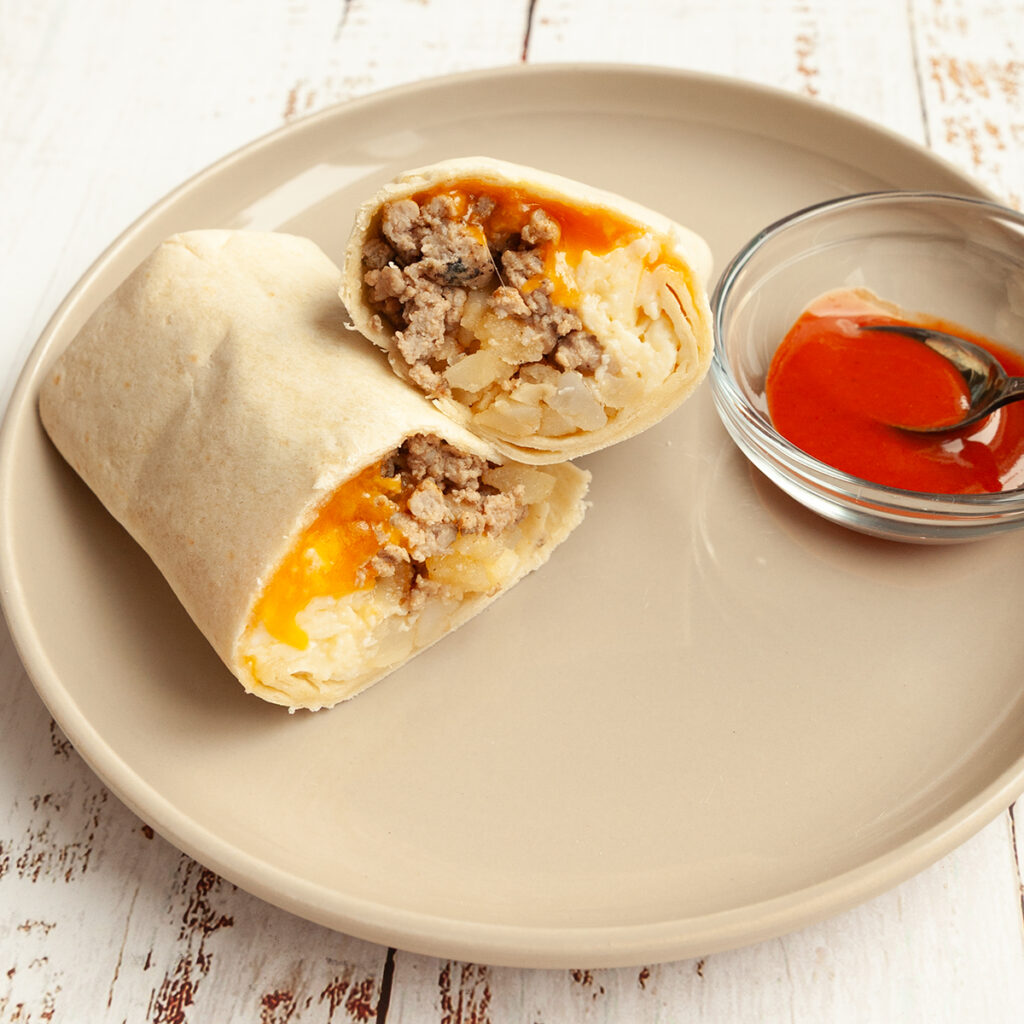 A breakfast burrito cut in half on a plate with hot sauce on the side.
