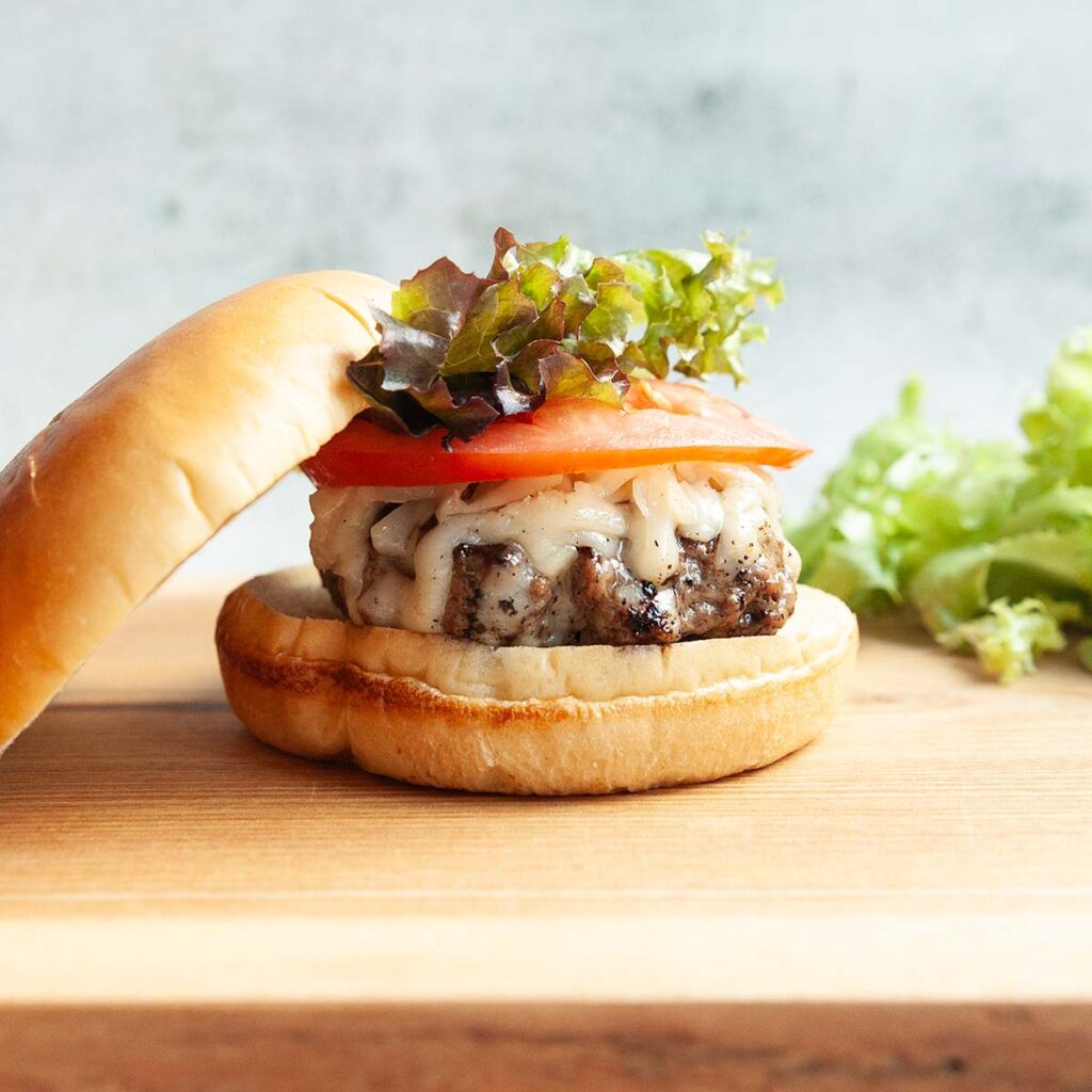 A burger topped with melted cheese, tomato, and lettuce.