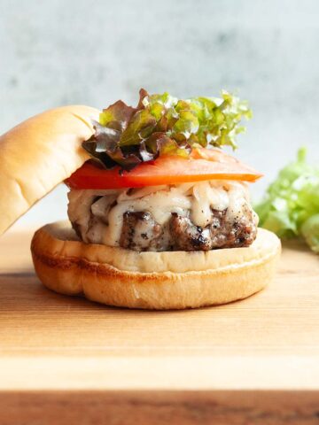 A burger topped with melted cheese, tomato, and lettuce.